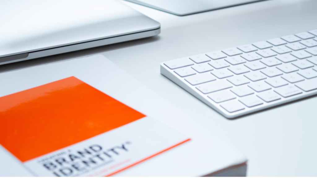 An image of a sleek, all-white digital workspace featuring a white book with orange accents titled 'Brand Identity' positioned in the bottom left corner. Reflective of the pivotal role that web design decisions play in shaping your brand's impact.