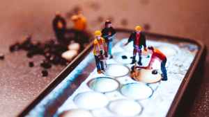 Construction worker figurines placed to look as though they are working on a cell phone screen.